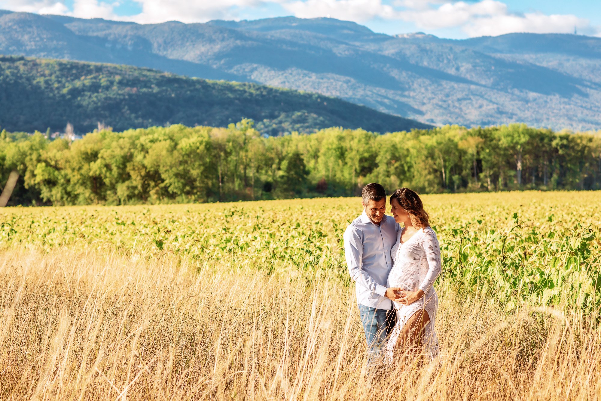 Couple embrace in outdoor maternity photo shoot with Jura Mountains behind