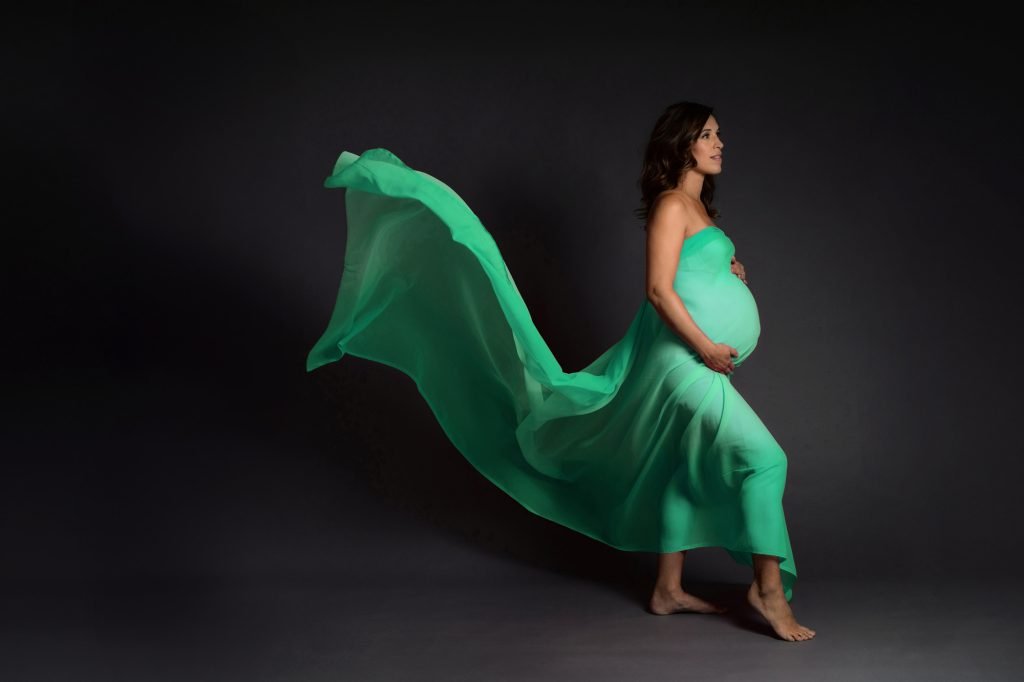 woman draped in green silk poses in maternity photo shoot, silk is floating on the breeze