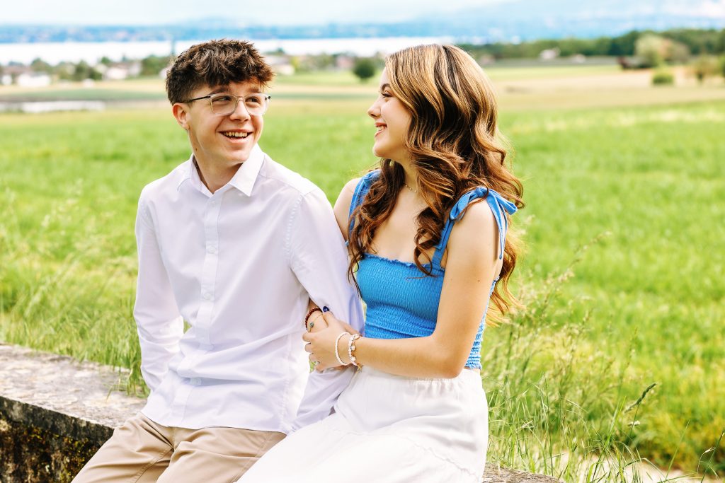 twins in their senior year in Nyon Switzerland sit together outside on a stone wall during a photo shoot for their senior pictures