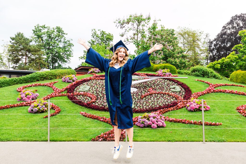 A young woman celebrating her high school graduation leaps for joy in front of the Jardin Anglais in Geneva