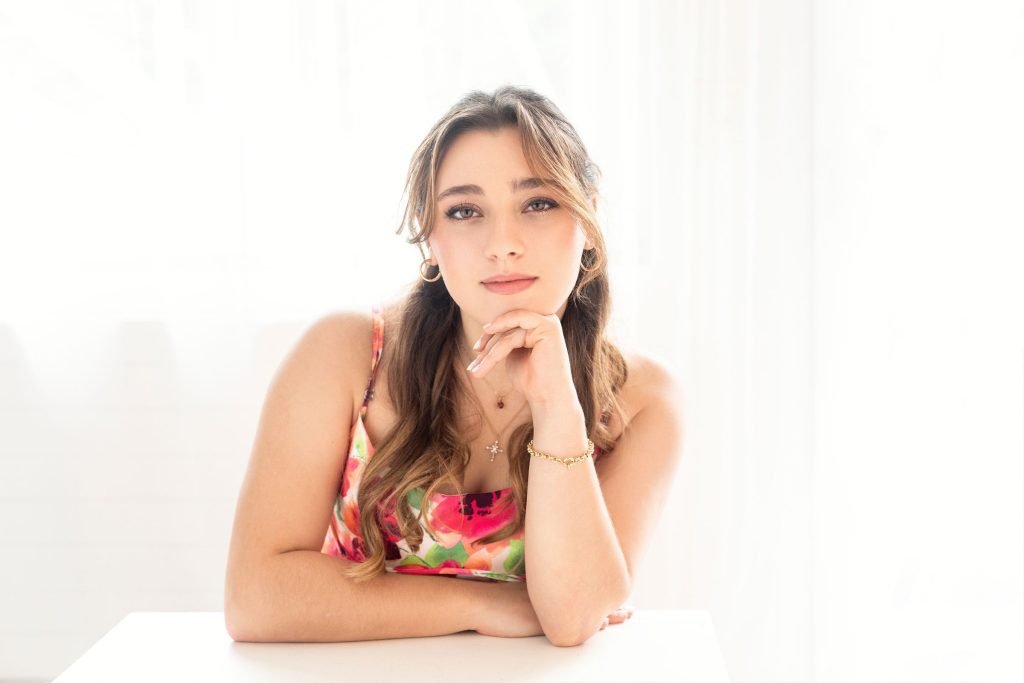 Image of a senior girl leaning on a table posing against a white background during her senior photo shoot session